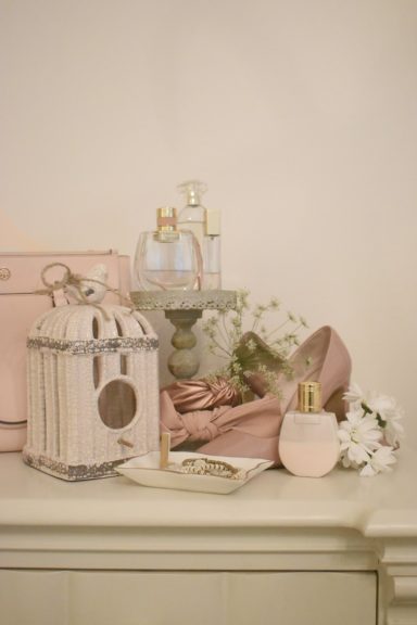 A decorative arrangement featuring cosmetics, flowers, and a birdcage on a table.